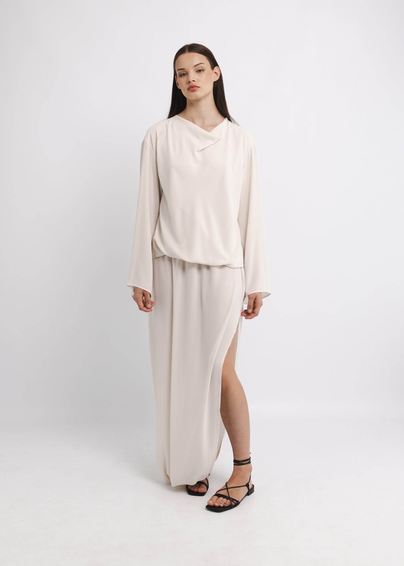 Woman wearing an ivory outfit with a draped top and long skirt on a white background